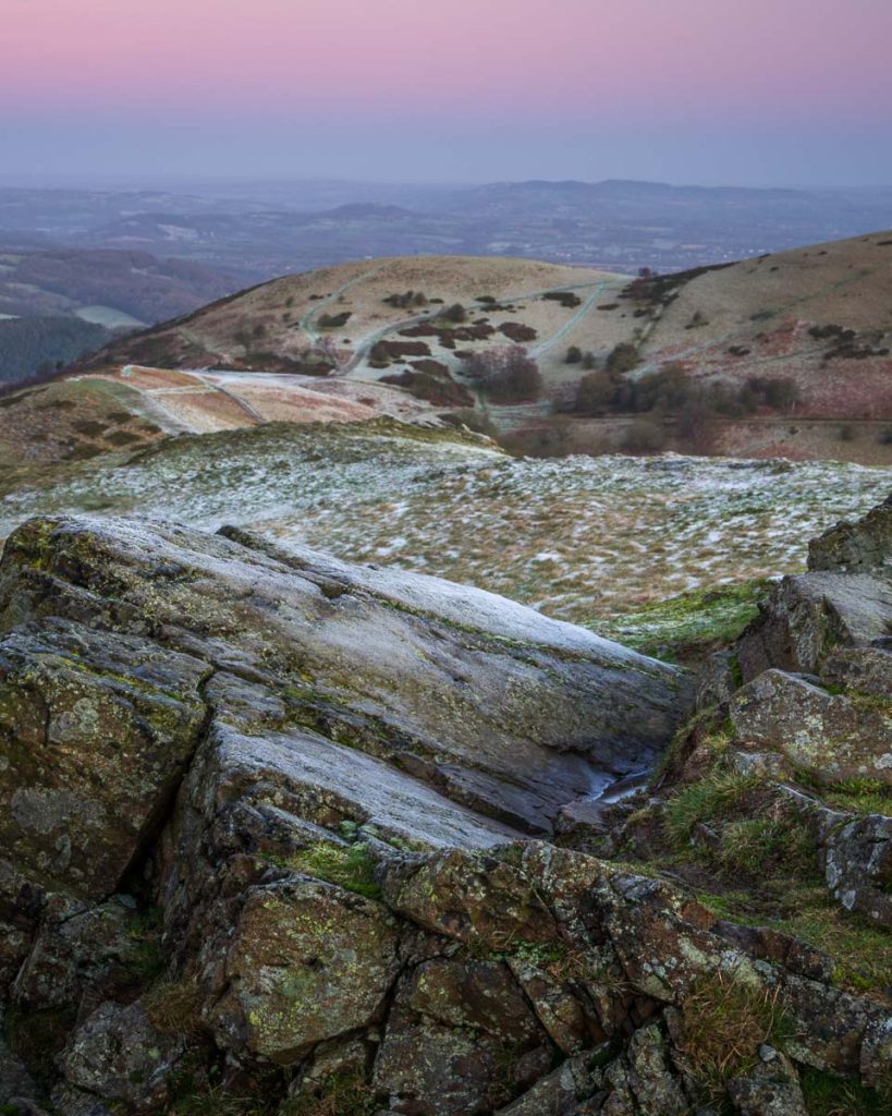 Frozen ground framed between foreground rocks and distant hills durning sunrise